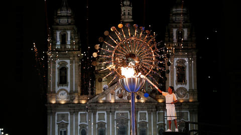 A person lights the Olympic Torch at night in front of a majestic castle. 