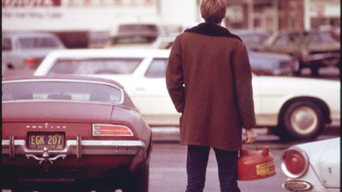 Back of a man in the 1970s standing to cars and holding a gas can