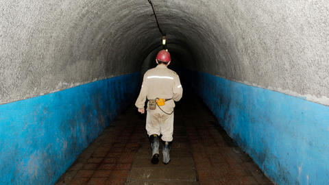 Back of coal miner in gear walking down a dark tunnel