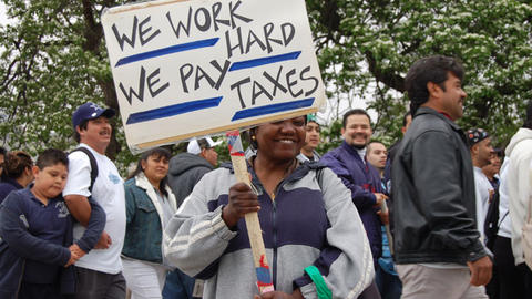 Image of woman holding a protest sign that says "We work hard. We pay our taxes."