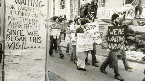 Black and white image of protesters carrying signs for Harvard to divest in Harvard Yard.