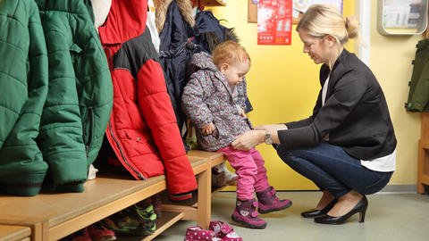 Image of woman helping child with coat in classroom