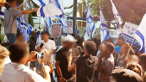 Antimigrant activists with Israeli flags surround asylum seekers while arguing and filming them.