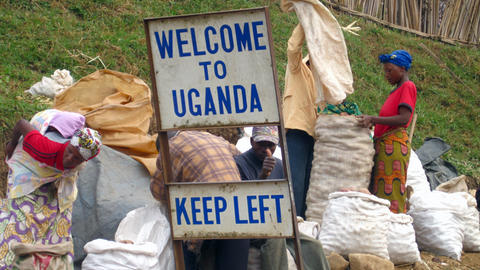 Refugees go through bags behind a "welcome to Uganda" sign
