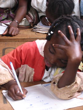 Image of a young girl at a school desk writing on a piece of paper.