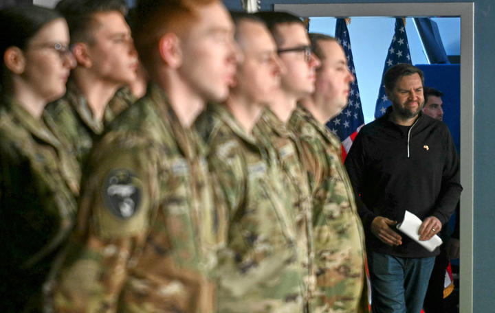 JD Vance stands in shadow behind a rows of soldiers.