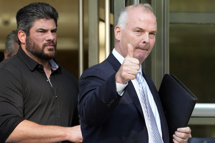 Balding man in a suit gives a thumbs up leaving a building.
