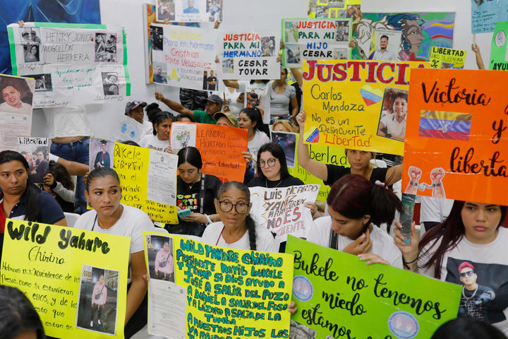 A crowd of deportees stands together holding up protest signs. 