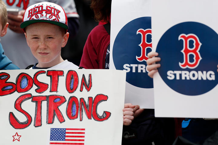 A boy wearing a baseball hat holds a handmade sign that says "Boston Strong" alongside other similar signs.