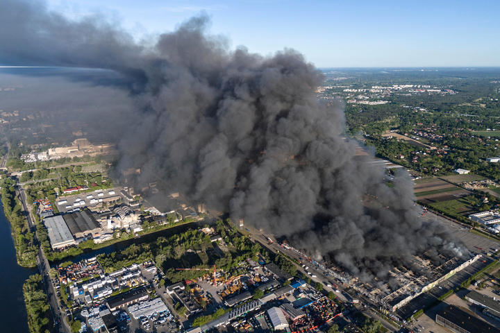 Overhead drone footage of a billowing cloud of dark gray smoke emanating from the city below. 