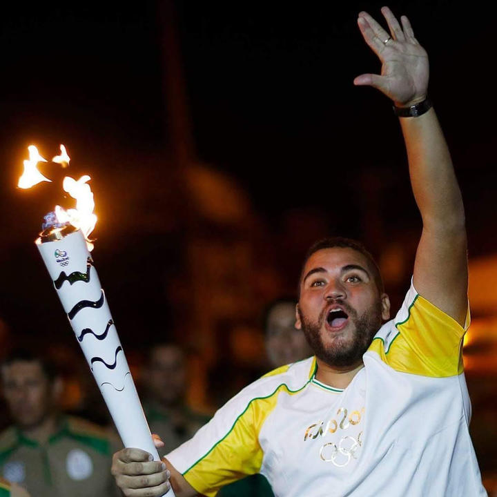 Man holding the Olympic Torch at night is raising up one arm in excitement. 