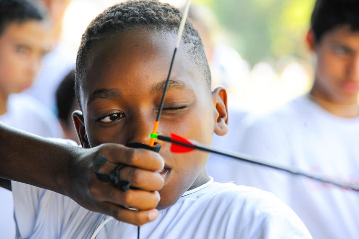 Close up of a boy pulling back the string of a bow, getting ready to shoot an arrow. 