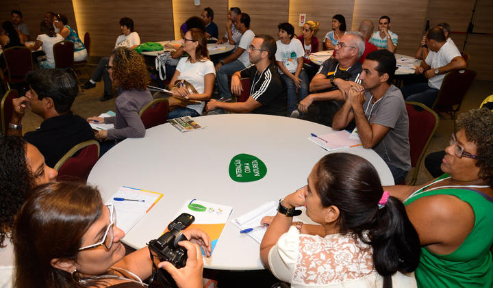 Dozens of teachers sit around circular tables during a teacher training. 