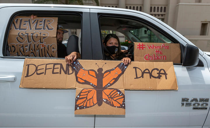 People in a car hold cardboard signs in and out of the window that say "Defend DACA" and "Never stop dreaming." 