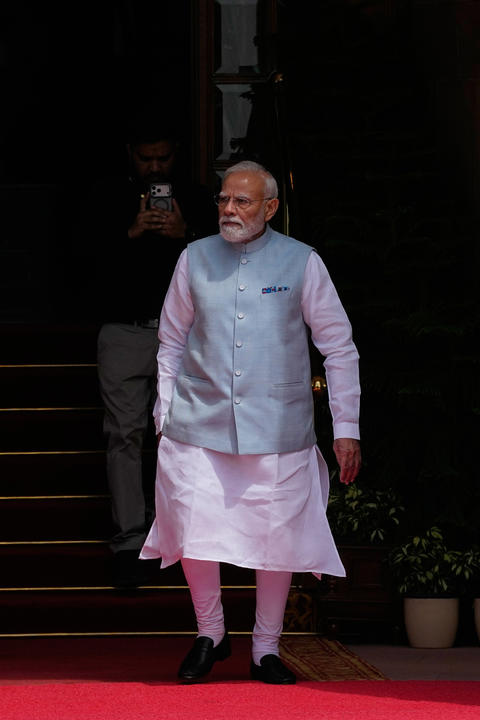 India's Prime Minister Narendra Modi walks on a red carpet at the bottom of steps. 