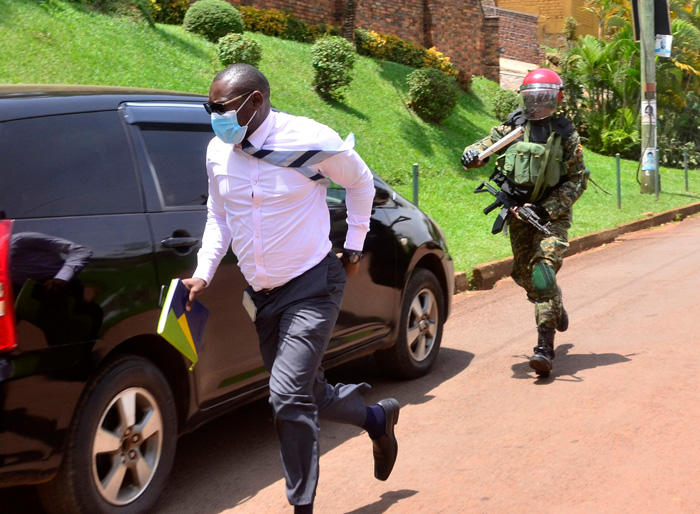 Journalist for Bobi Wine, in a suit, running from a police officer