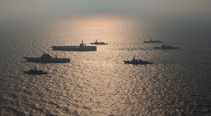 Overhead view of 7 naval ships in the ocean at sunrise