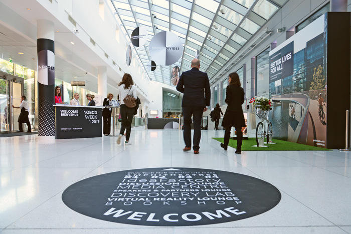 The backs of people walking down a hall toward a welcome desk for the OECD 2017 meeting.