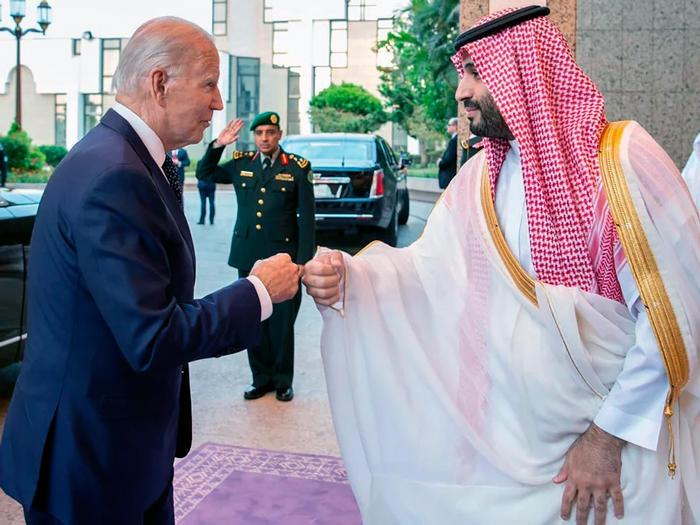President Joe Biden and Saudi Crown Prince Mohammed bin Salman bin Abdulaziz bump fists on the street outside Al-Salam Palace while a soldier gives a salute in the background.