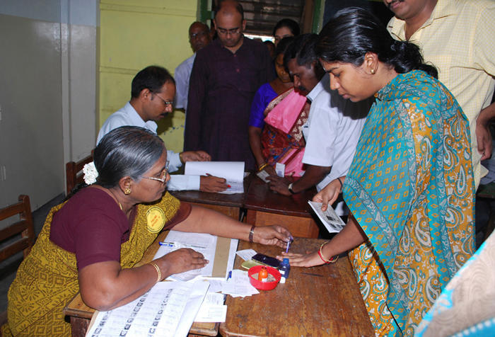 Polling officer sitting at a table administers indelible ink on the finger of a female voter at Tamil Nadu