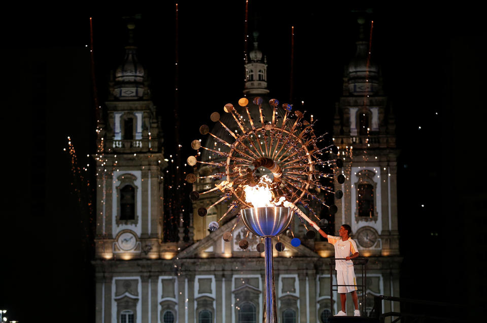 A person lights the Olympic Torch at night in front of a majestic castle. 