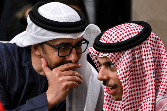 Two Middle Eastern me leaning in toward each other and whispering.